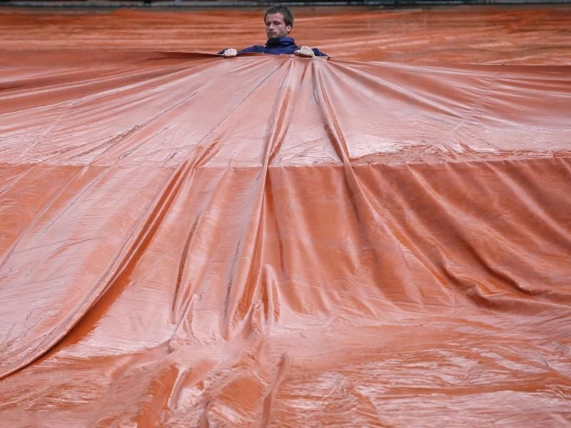 Ein Stadionarbeiter zieht eine Folie über den Platz. Foto: Thibault Camus/AP
