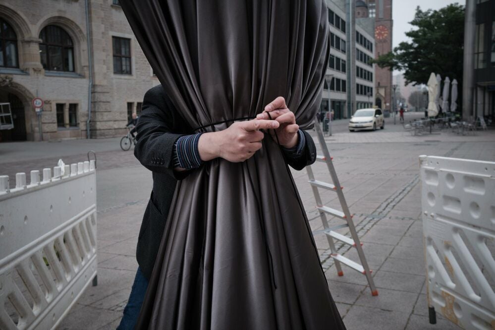 Das Bild zeigt die Hände von Christopher Melching beim Verpacken der Statue. Melching ist Leiter der Kostümwerkstätten am Anhaltischen Theater, in denen die Denkmalhülle genäht wurde.