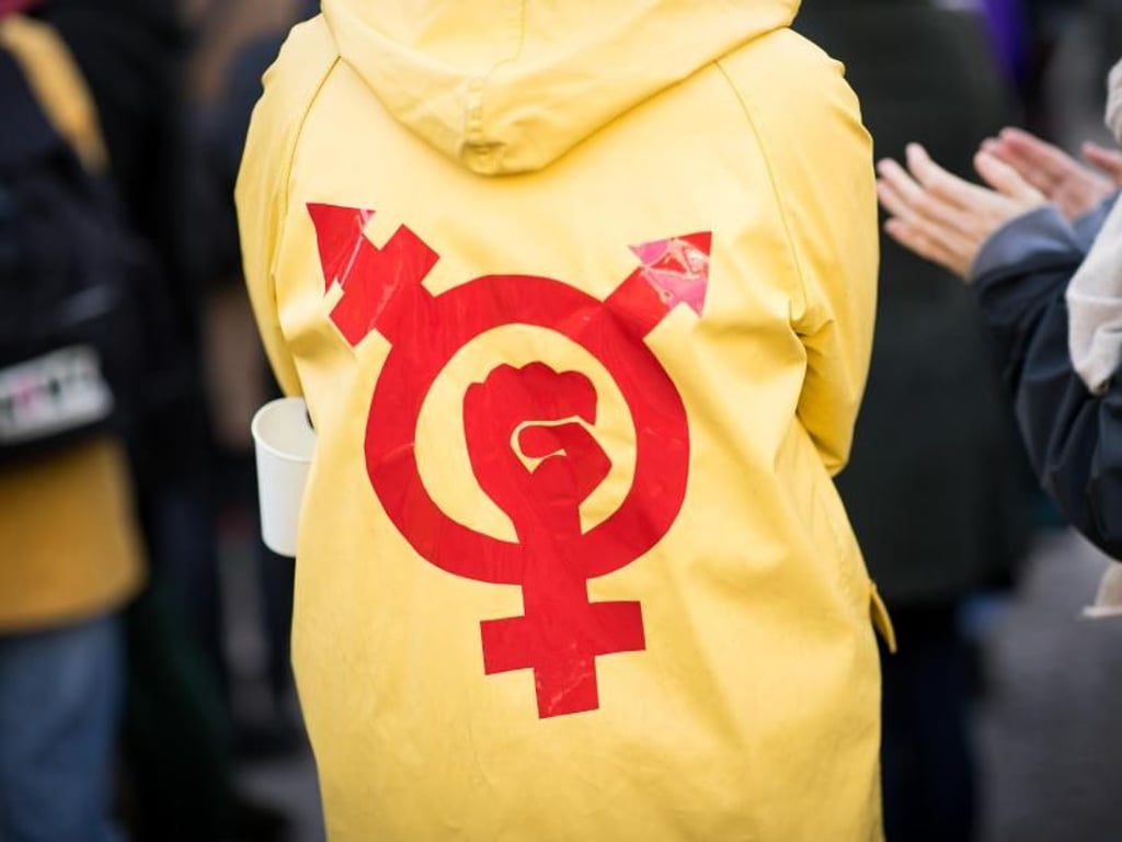 Eine Frau trägt einen Regenmantel mit einem Gender- und Protestsymbol bei einer Kundgebung. Die Diskussion um das Gendern wird immer populärer in Deutschland.