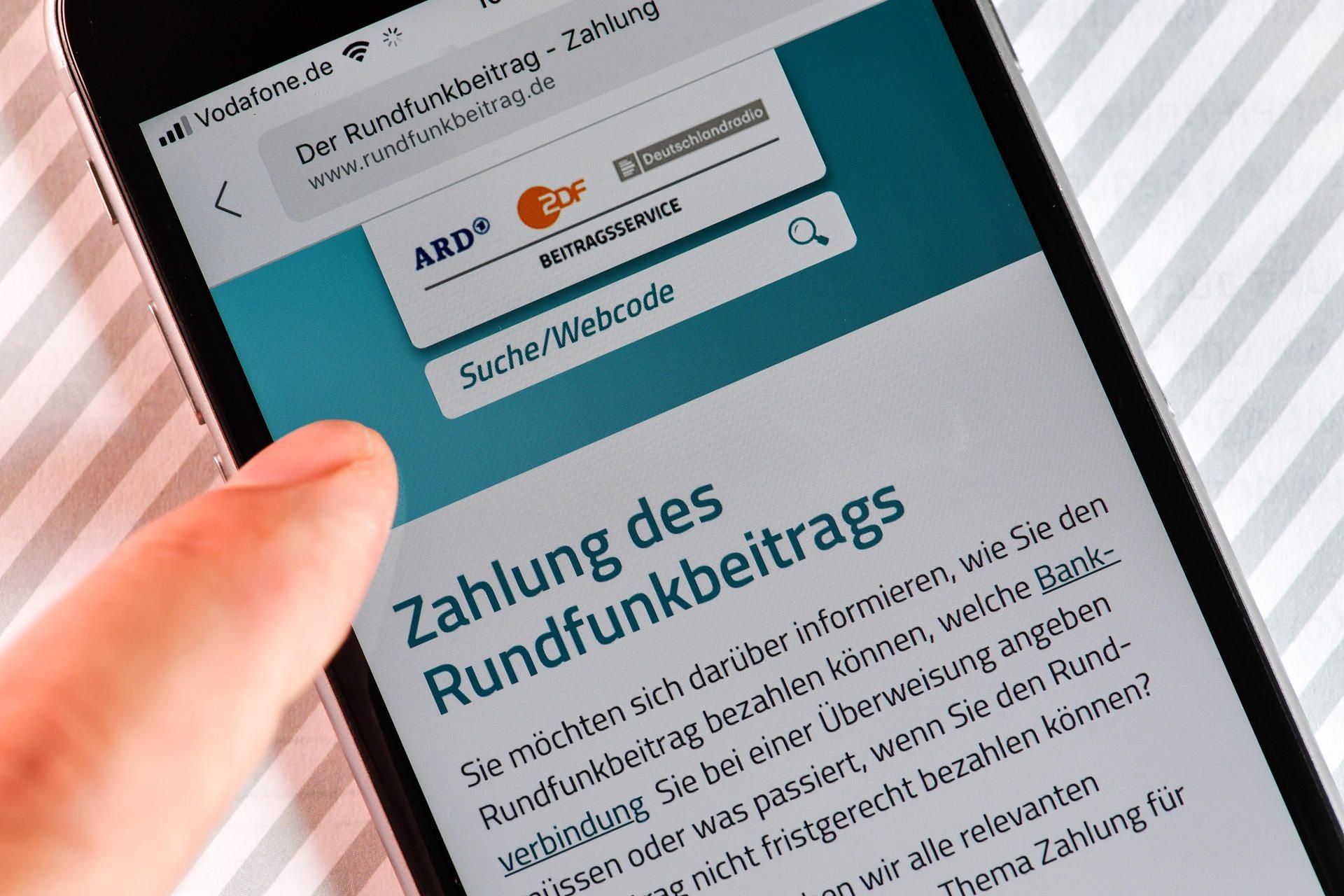 Auf einem Smartphone ist eine Website zur Information über die Zahlung des Rundfunkbeitrags aufgerufen. Hier kann man auch Formulare für die Überweisung herunterladen.