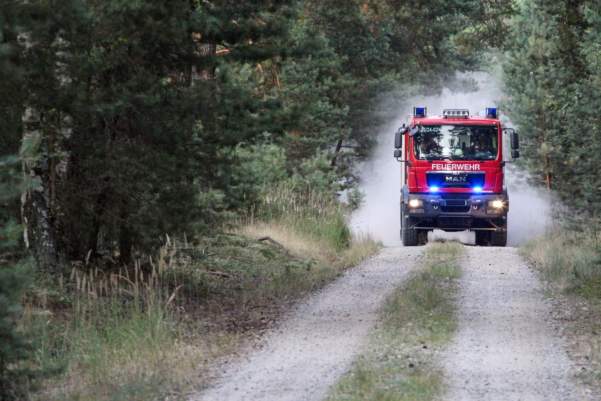 Ein Löschfahrzeug der Feuerwehr fährt zu einem Einsatz in einem Waldgebiet. Gefahrenquelle für Waldbrände können auch Erntearbeiten sein.