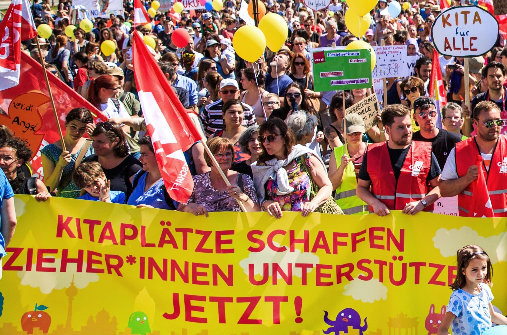 Demonstranten halten ein Transparent mit dem Aufdruck "Kitaplätze schaffen Erzieherinnen unterstützen jetzt !" während Eltern und Erzieher für mehr Plätze in den Kitas und eine bessere Bezahlung der Erzieher in Berlin demonstrieren.
