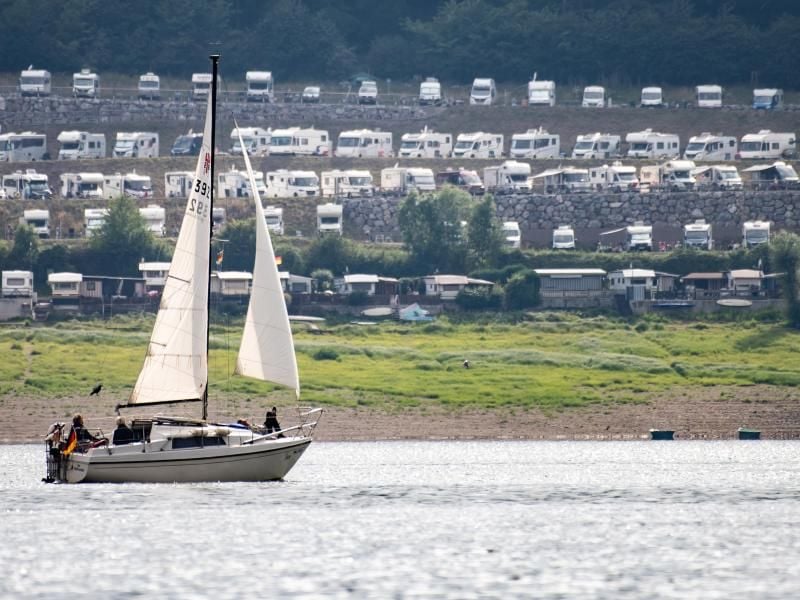 Ein Segelboot ist auf dem Edersee vor zahlreichen Wohnmobilen unterwegs. Foto: Swen Pförtner/dpa
