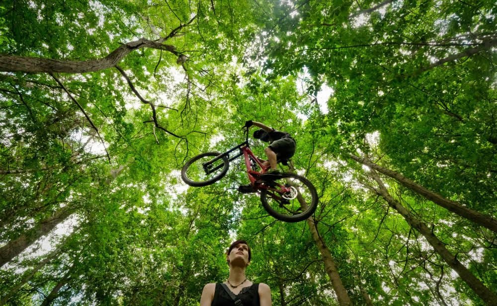 Jugendliche haben sich im Trothaer Wald eine Mountainbike-Strecke aufgebaut. Robert springt mit dem Rad über seine Freundin.