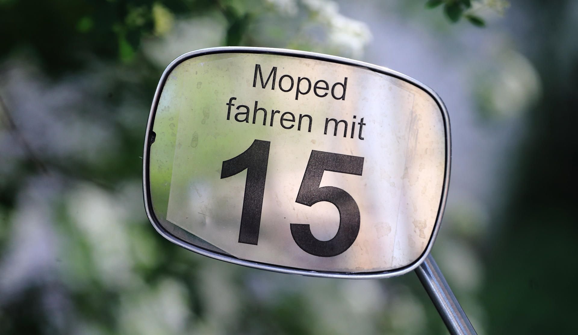 Der Schriftzug „Moped fahren mit 15“ ist an dem Spiegel eines Mopeds angebracht
