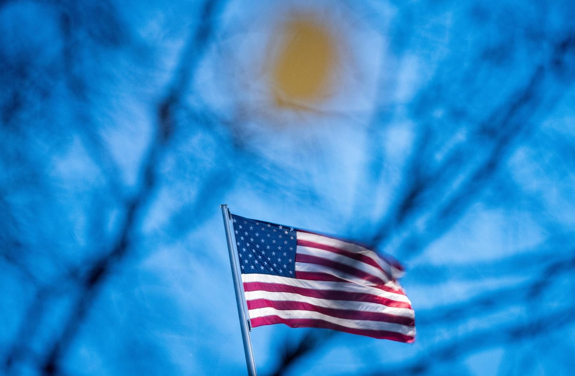 Die Flagge der Vereinigten Staaten von Amerika weht auf der US-Botschaft hinter den Ästen eines Baumes im Wind in Berlin.