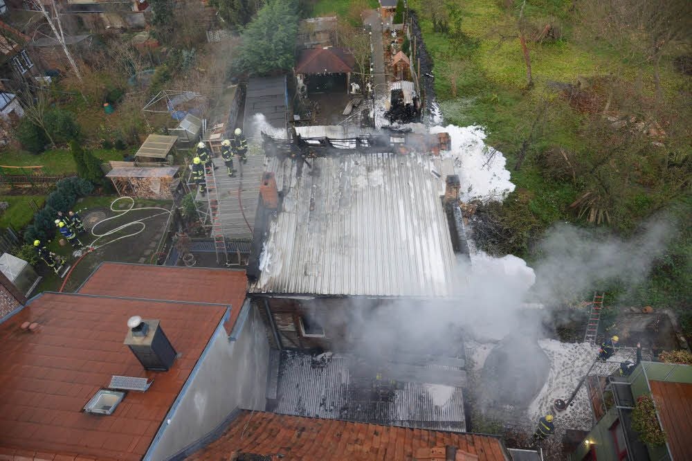 Blick von oben auf das brennende Haus und einen Schuppen.