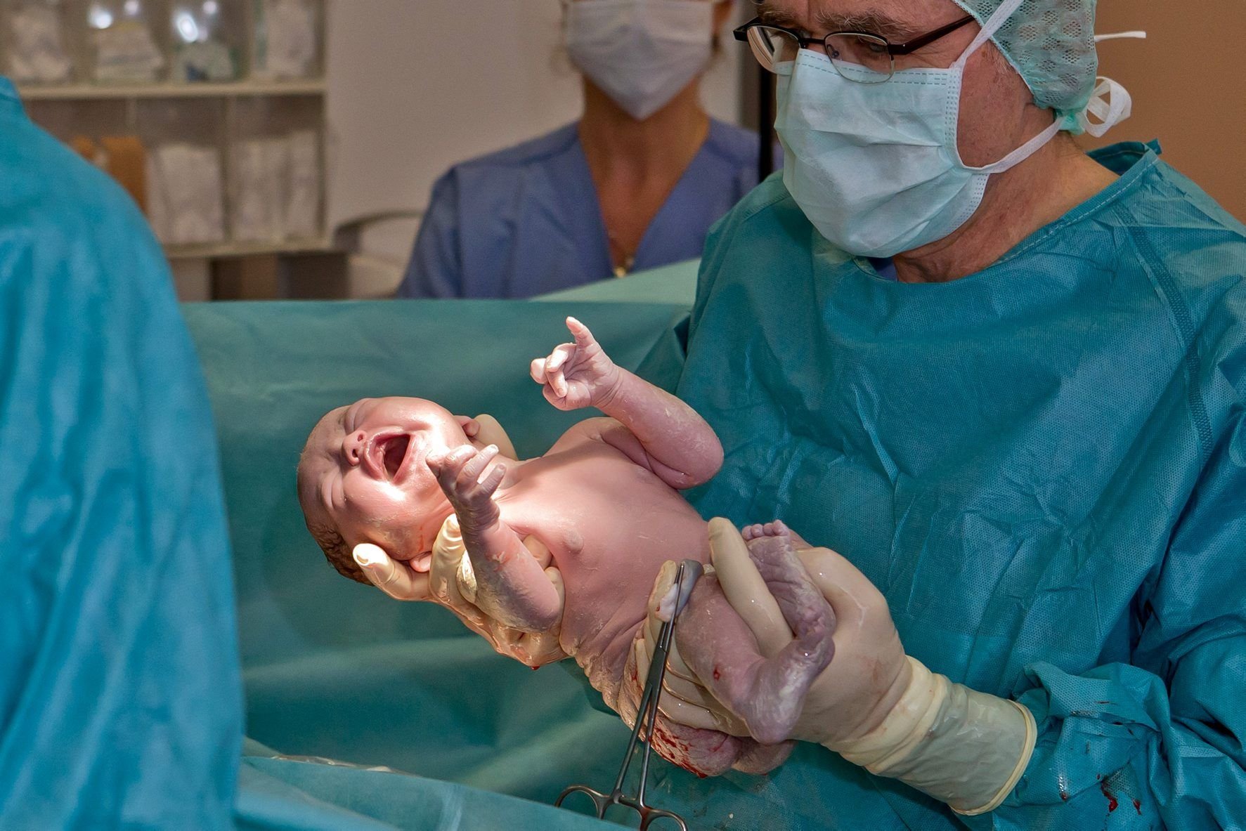 Ein Arzt hält im Kreißsaal einer Frauenklinik ein Baby in den Händen, das per Kaiserschnitt zur Welt kam.