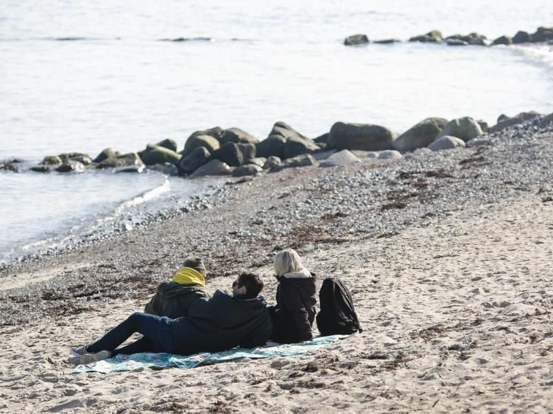 Drei Personen bei sonnigem Wetter am Strand in Strande. Foto: Frank Molter/dpa