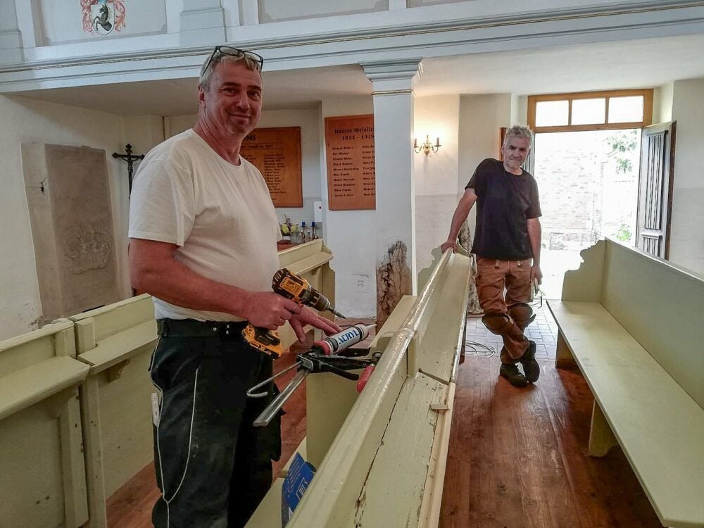 Die Zimmerleute Maik Naundorf und Marco Drechsler bessern Teile der Holzbänke in der Kirche Predel aus.