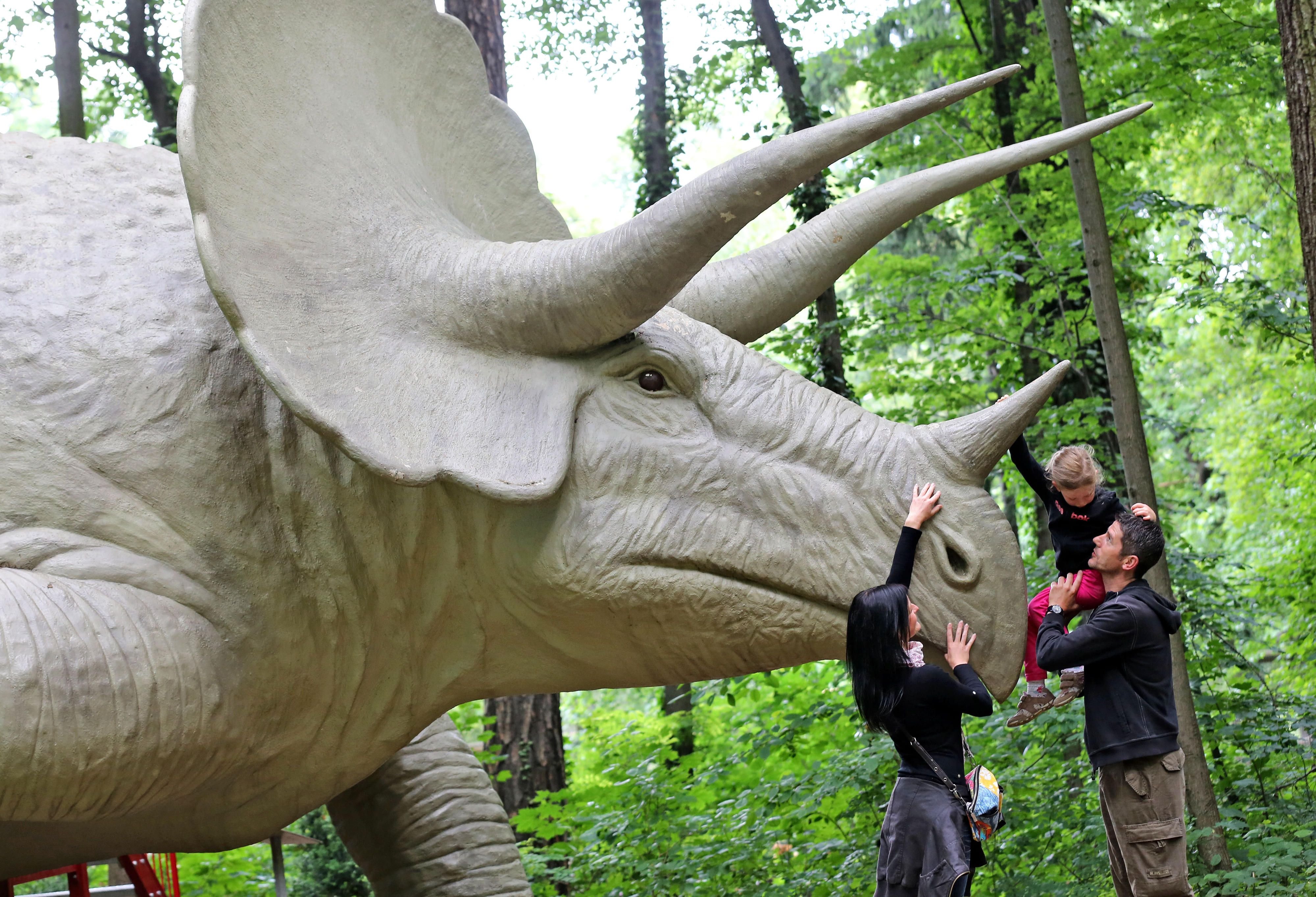 Die kleine Anna klettert mit Hilfe ihrer Eltern Eileen Arnold und Holger Schmidt auf einen riesigen Triceratops im Saurierpark Kleinwelka bei Bautzen.