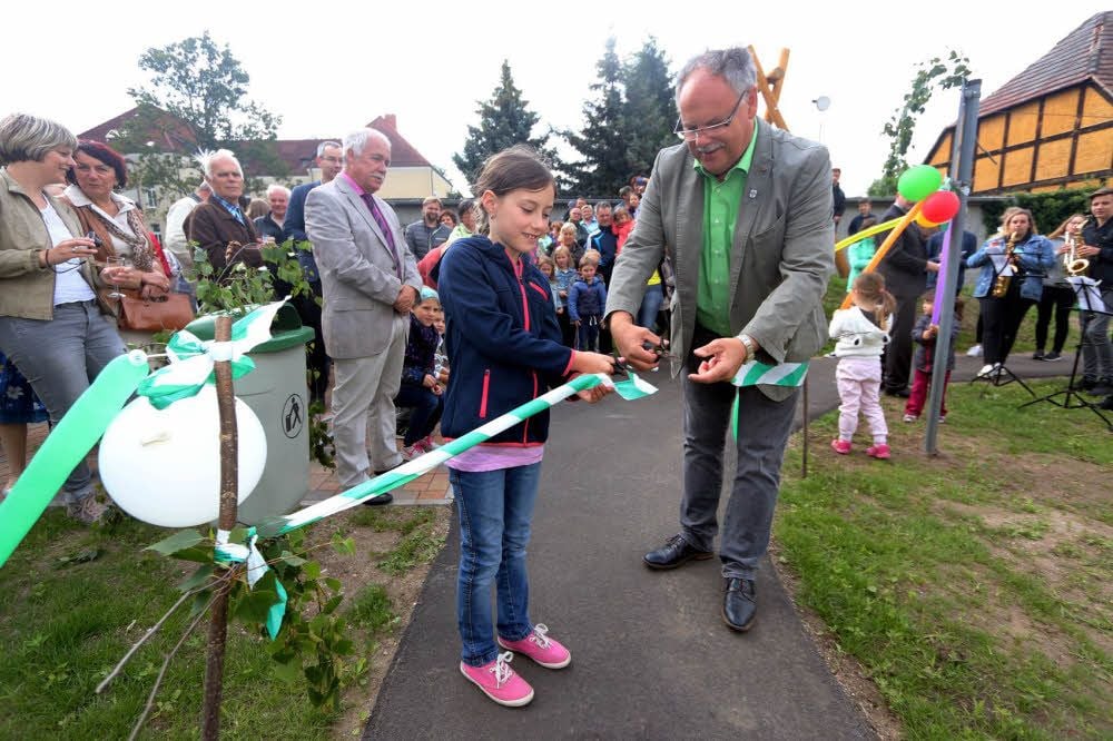 Gemeinsam mit der neunjährigen Lea gibt Bürgermeister Klaus-Rüdiger Neubauer den Weg zum neuen Spielplatz in Annaburg frei.
