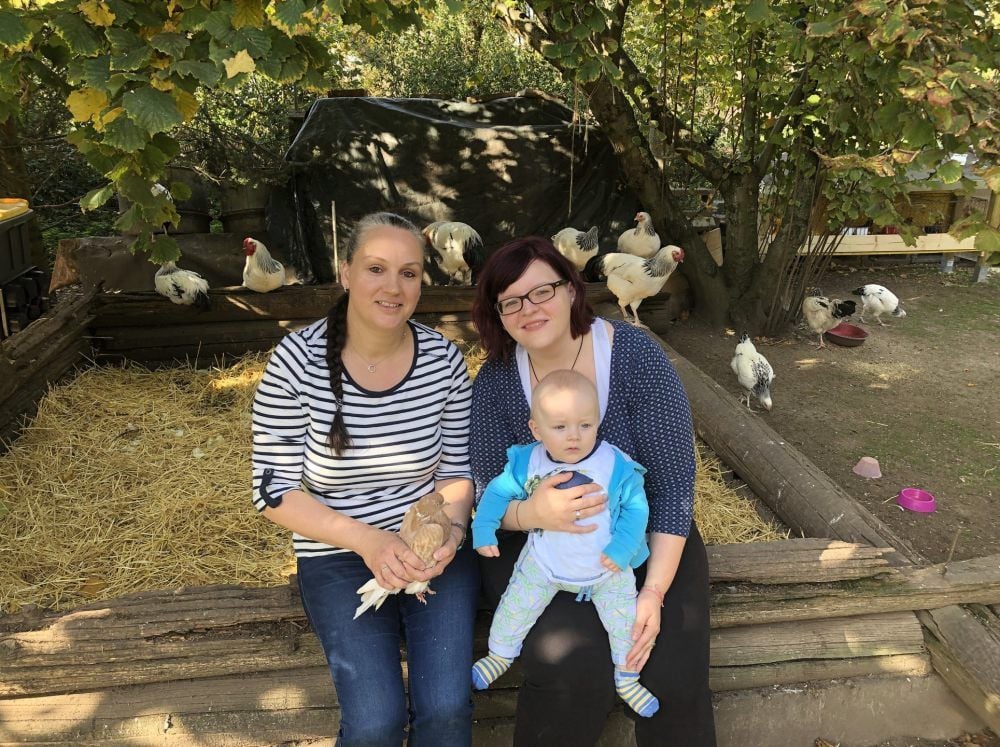 Kerstin Isbarn und Sophie Hendeß und Ihr Söhnchen Arian sitzen im Gehege der Deutschen Reichshühner.