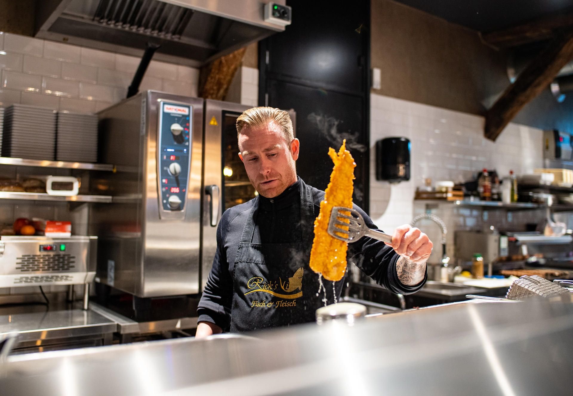 Inhaber Rick de Vries steht hinter seiner Fischtheke und nimmt einen Backfisch aus dem heißen Fett.