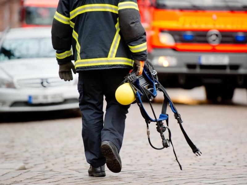 Ein Feuerwehrmann trägt ein Atemschutzgerät zum Fahrzeug. Foto: Daniel Bockwoldt/Archiv