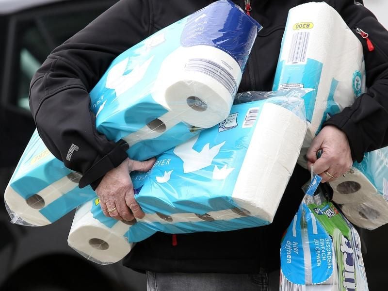 Ein Mann trägt Toilettenpapier und Küchenrollen aus einem Supermarkt. Foto: Rene Traut/dpa