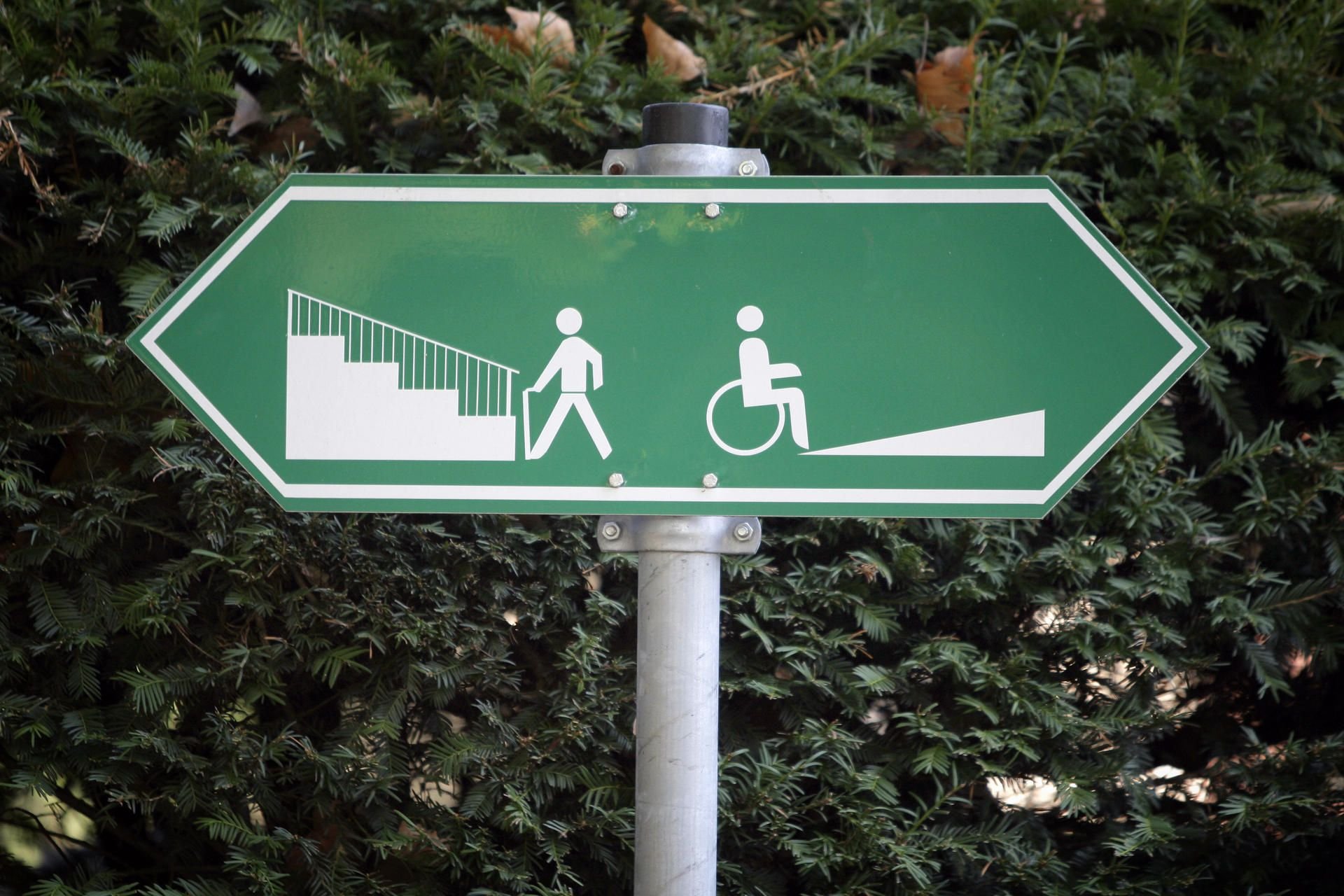 Ein Schild weist darauf hin, dass Fußgänger links eine Treppe und Rollstuhlfahrer rechts eine Auffahrt benutzen können.