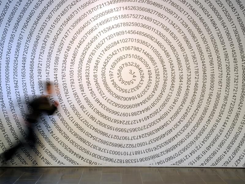 Ein Schulkind läuft im Mitmachmuseum „Mathematikum” an der auf eine Wand geschriebenen Kreiszahl Pi vorbei. Foto: Uwe Zucchi/Archivbild
