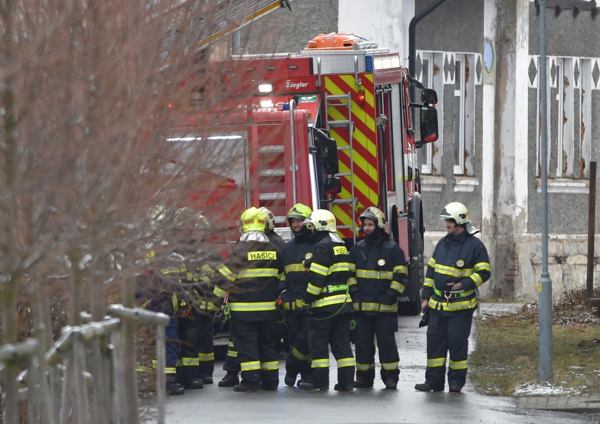 Feuerwehrleute stehen während der Löscharbeiten an einem Einsatzwagen vor einem Pflegeheim für Behinderte.