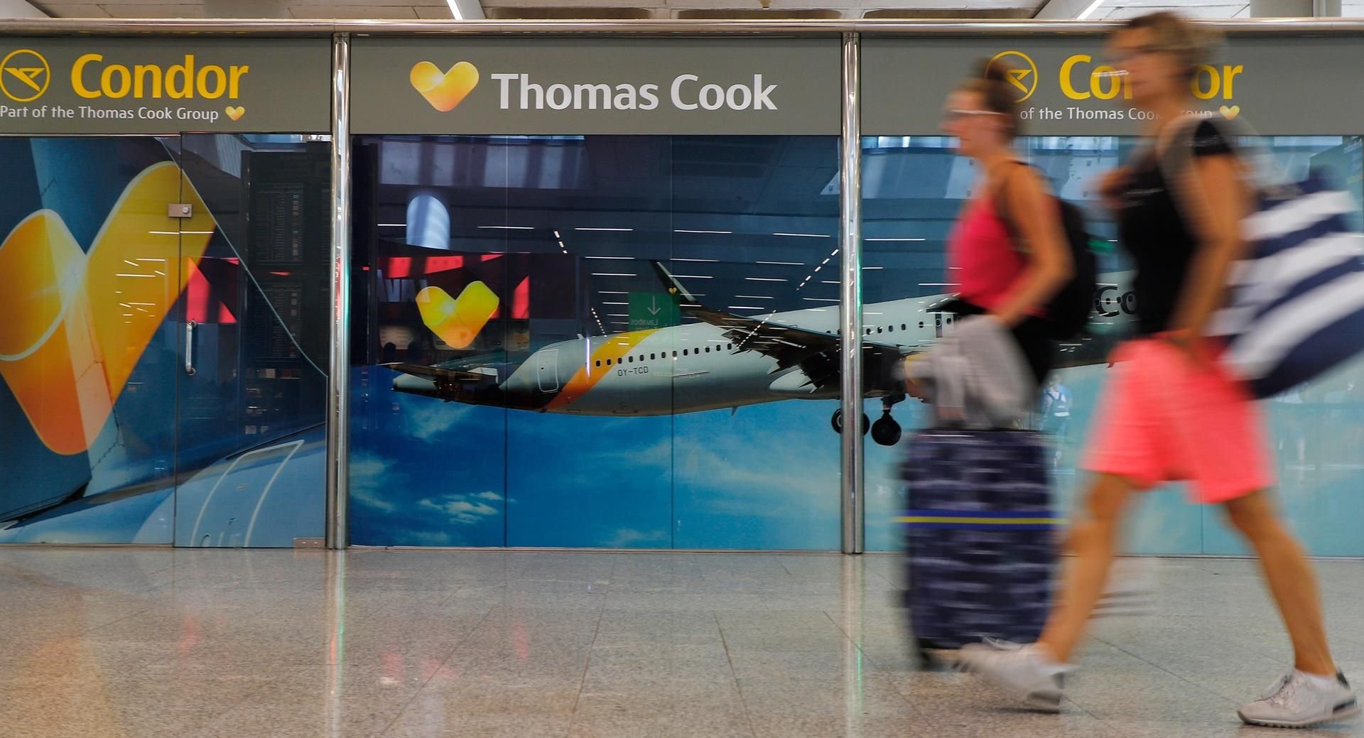 Passagiere gehen neben einem großen Werbeschild von Thomas Cook am Flughafen von Palma de Mallorca.