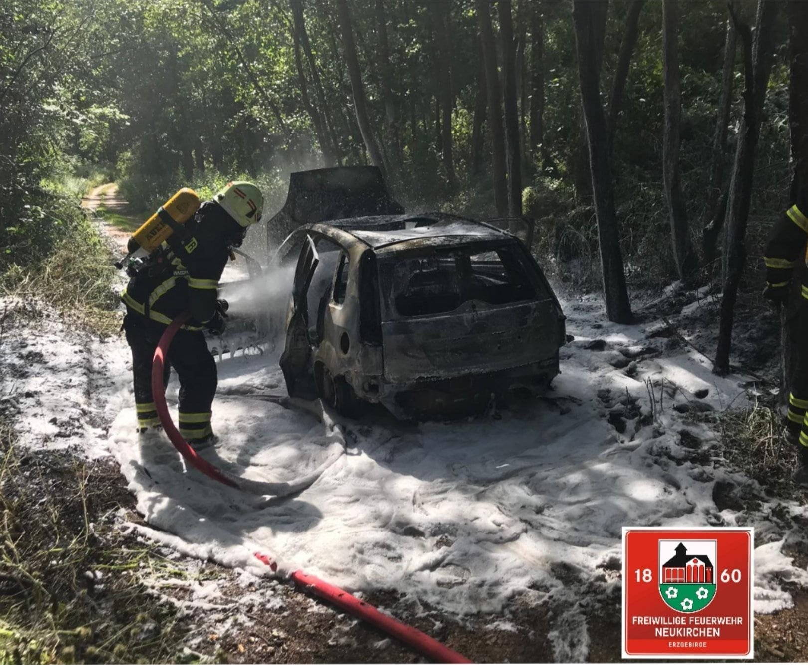 Ein Mitglied der Freiwilligen Feuerwehr Neukirchen/Erzgebirge löscht das brennende Auto.