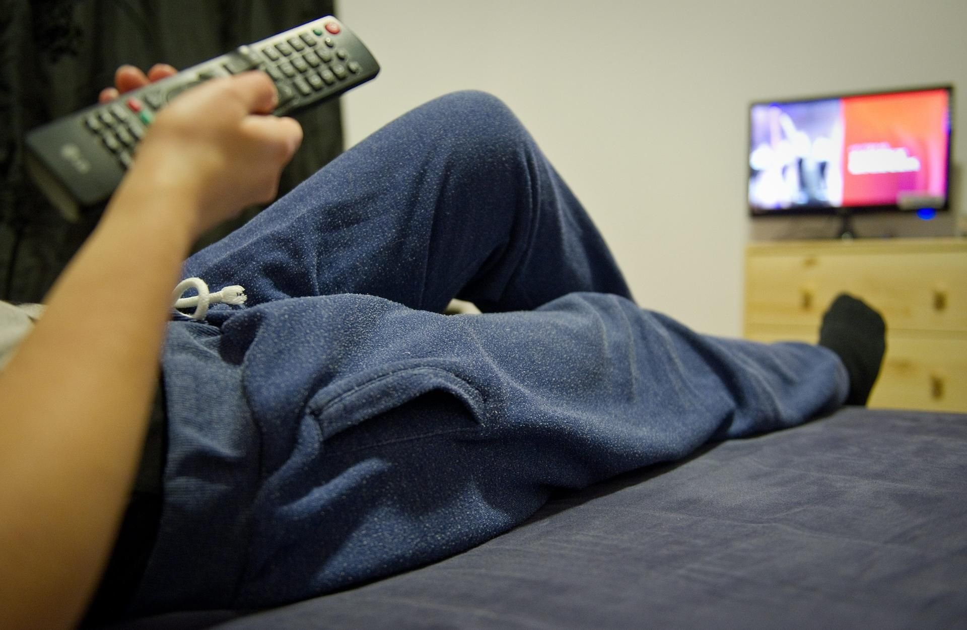 Eine junge Frau trägt vor dem Fernseher eine Jogginghose.