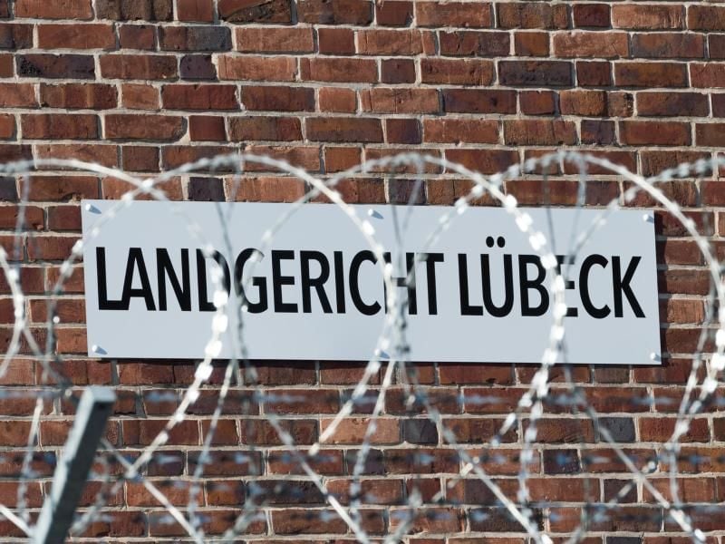 Ein Schild mit der Aufschrift „Landgericht Lübeck” an der Außenwand hinter Stracheldraht. Foto: Christophe Gateau/dpa/Archivbild