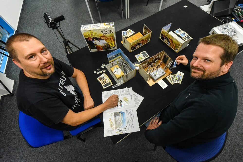 Robert Letsch (l.) und Frank Noack sitzen beim Spiel „Der perfekte Moment“ an dem Tisch, wo zur Messe die Spielrunden übertragen wurden.