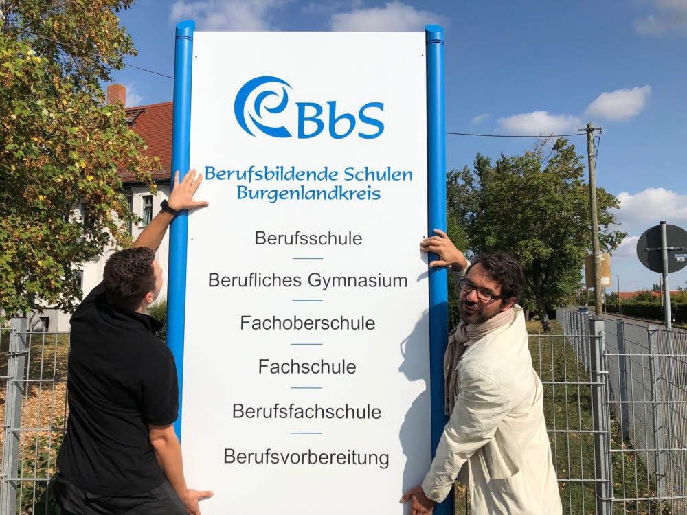Das Fachgymnasium heißt jetzt Berufliches Gymnasium. Schulleiter Jörg Riemer (re.) bringt mit Werbetechniker Markus Ritter das neue Schild an.