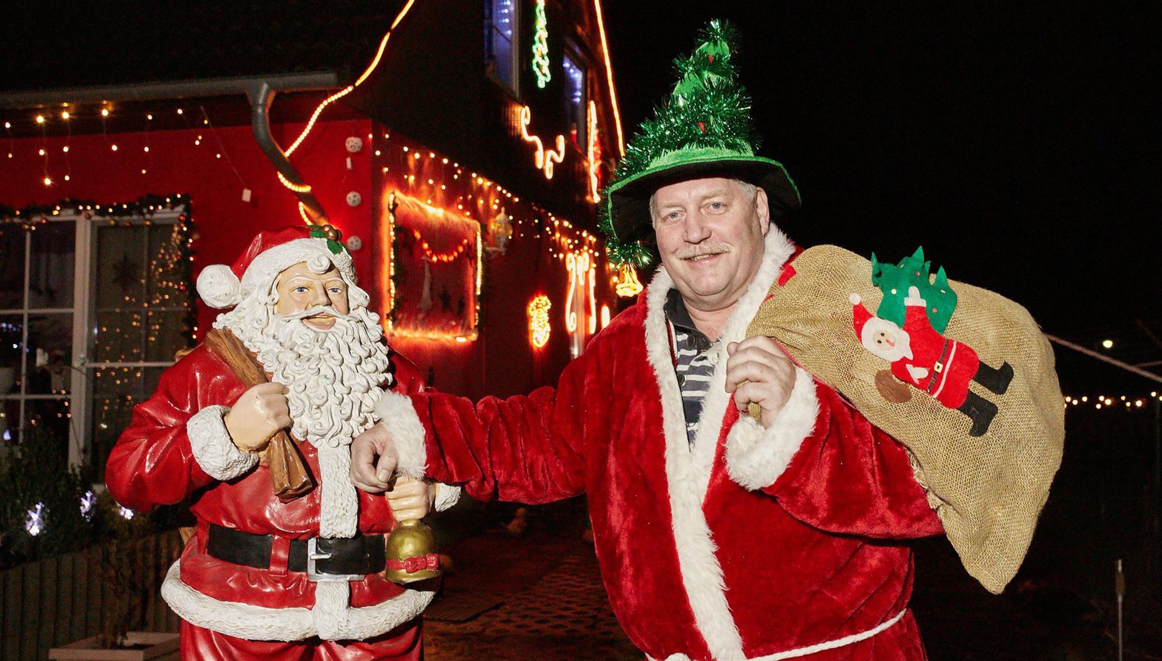 Bernd Meyer steht vor seinem weihnachtlich geschmückten Haus und zeigt die Weihnachtsmann-Figur mit der seine Leidenschaft anfing.