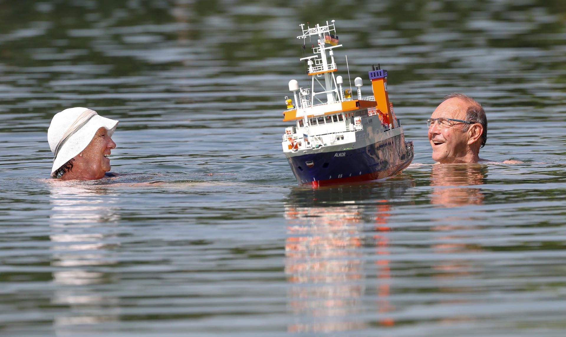 Spaß im kühlen Nass: Ein Ehepaar schwimmt in einem See an einem Modellboot vorbei.