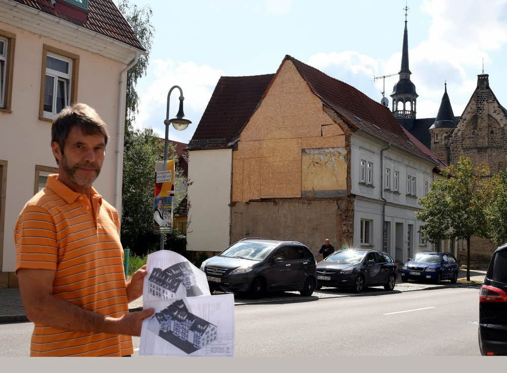 Thomas Luft, Technischer Angestellter der Wohnbau Lützen GmbH, zeigt Pläne für die seniorengerechten Wohnungen, die in der Baulücke in der Ernst-Thälmann-Straße (im Hintergrund) entstehen sollen.