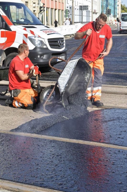 Gussasphalt zwischen Straßenbahngleisen wird manuell eingebaut.