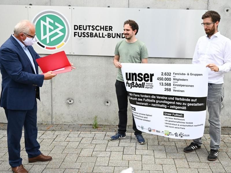 Jan-Henrik Gruszecki (r) und Manuel Gaber (M) von der Fan-Initiative „Unser Fußball” übergeben eine Erklärung zur geforderten Reform an DFB-Präsident Fritz Keller. Foto: Arne Dedert/dpa