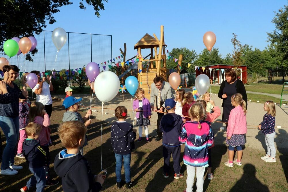 Das Band wird zerschnitten, das den Weg freigibt zum neuen Kletterturm im Spielgarten der Kindertagesstätte „Birkengrund“ in Schweinitz. Zeitgleich lassen Mädchen und Jungen Luftballons steigen.