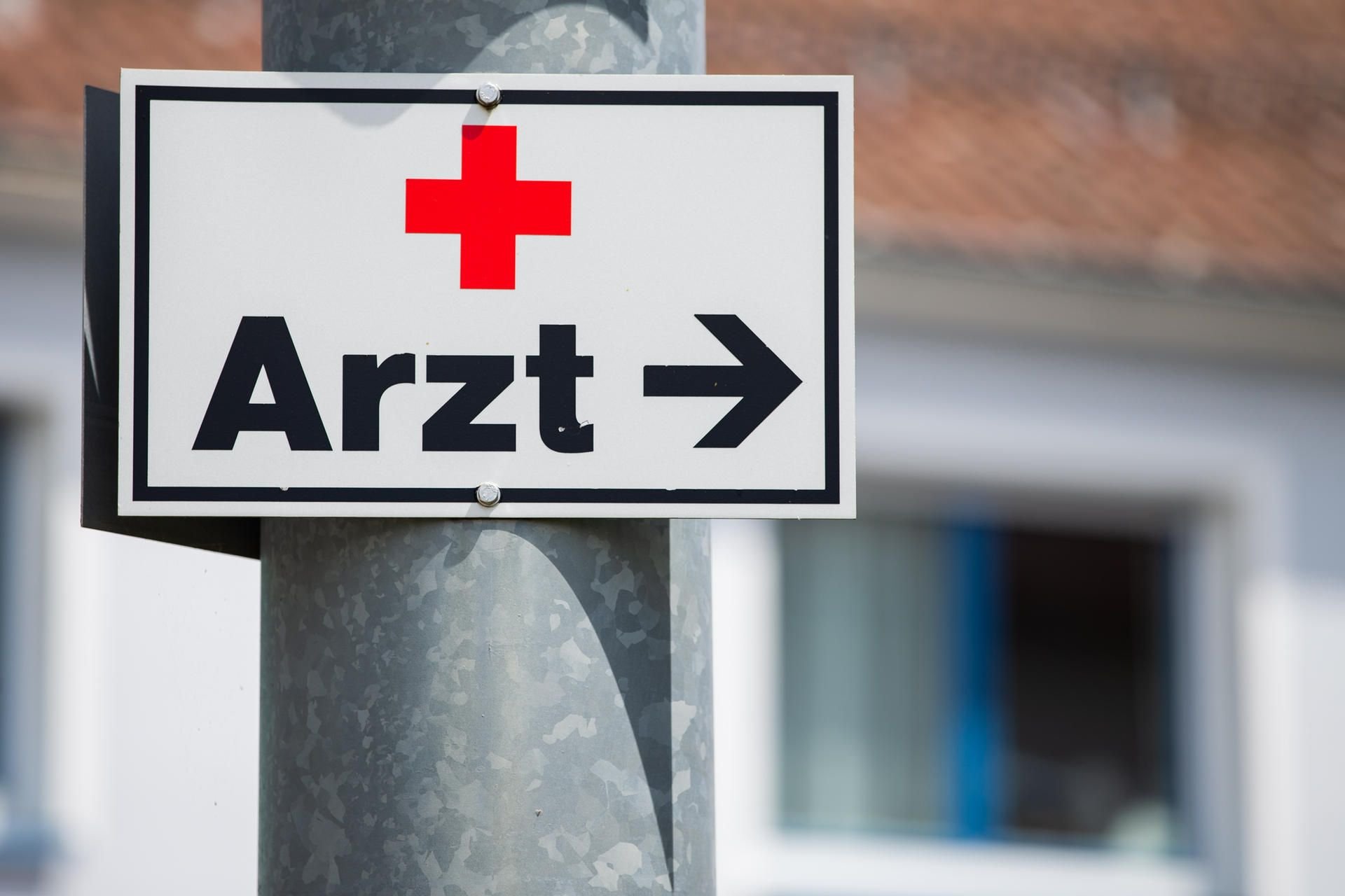Ein Schild mit Pfeil und der Aufschrift „Arzt“ hängt an einer Straßenlaterne.