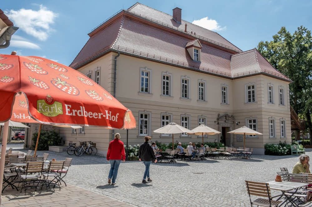 Im Freisitz des Gutshauses erinnern Erdbeer-Sonnenschirme an die Verbindung zu „Karls“.