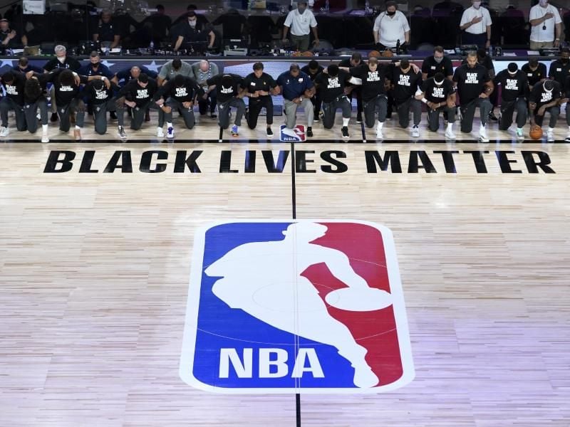Alle Spieler der New Orleans Pelicans und von Utah Jazz knien vor einem „Black Lives Matter”-Schriftzug. Foto: Ashley Landis/Pool AP/dpa