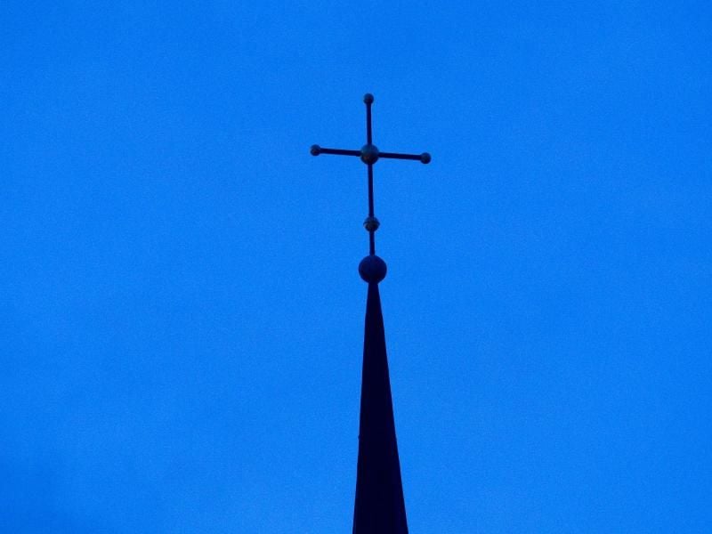 Ein Kreuz ist auf einer Kirchturmspitze zu sehen. Foto: Friso Gentsch/dpa/Symbolbild