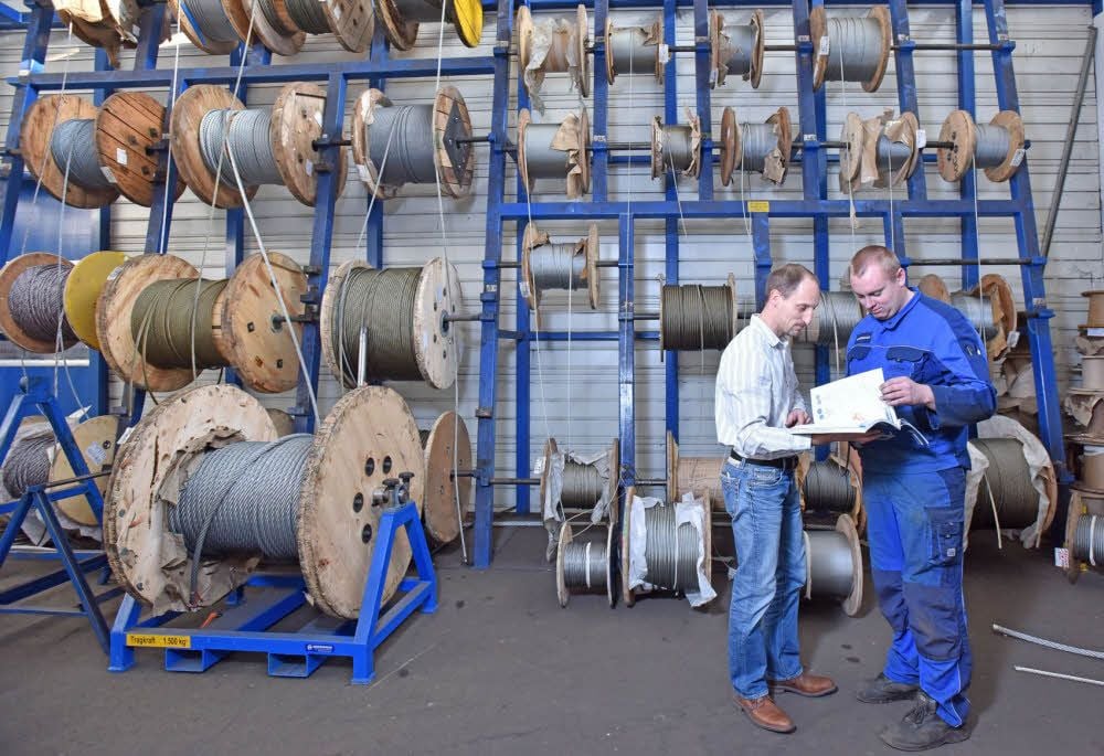 Produktionsmanager Michael Bauer (l.) und Mitarbeiter Phillip Ptak vorm Regal mit Rollen von Stahlseilen mit verschiedenen Durchmessern