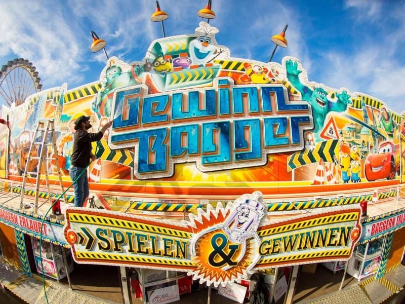 Ein Arbeiter putzt den Schriftzug „Gewinn Bagger” an seinem Spielgeschäft auf dem Hamburger Dom. Foto: Christian Charisius/Archiv
