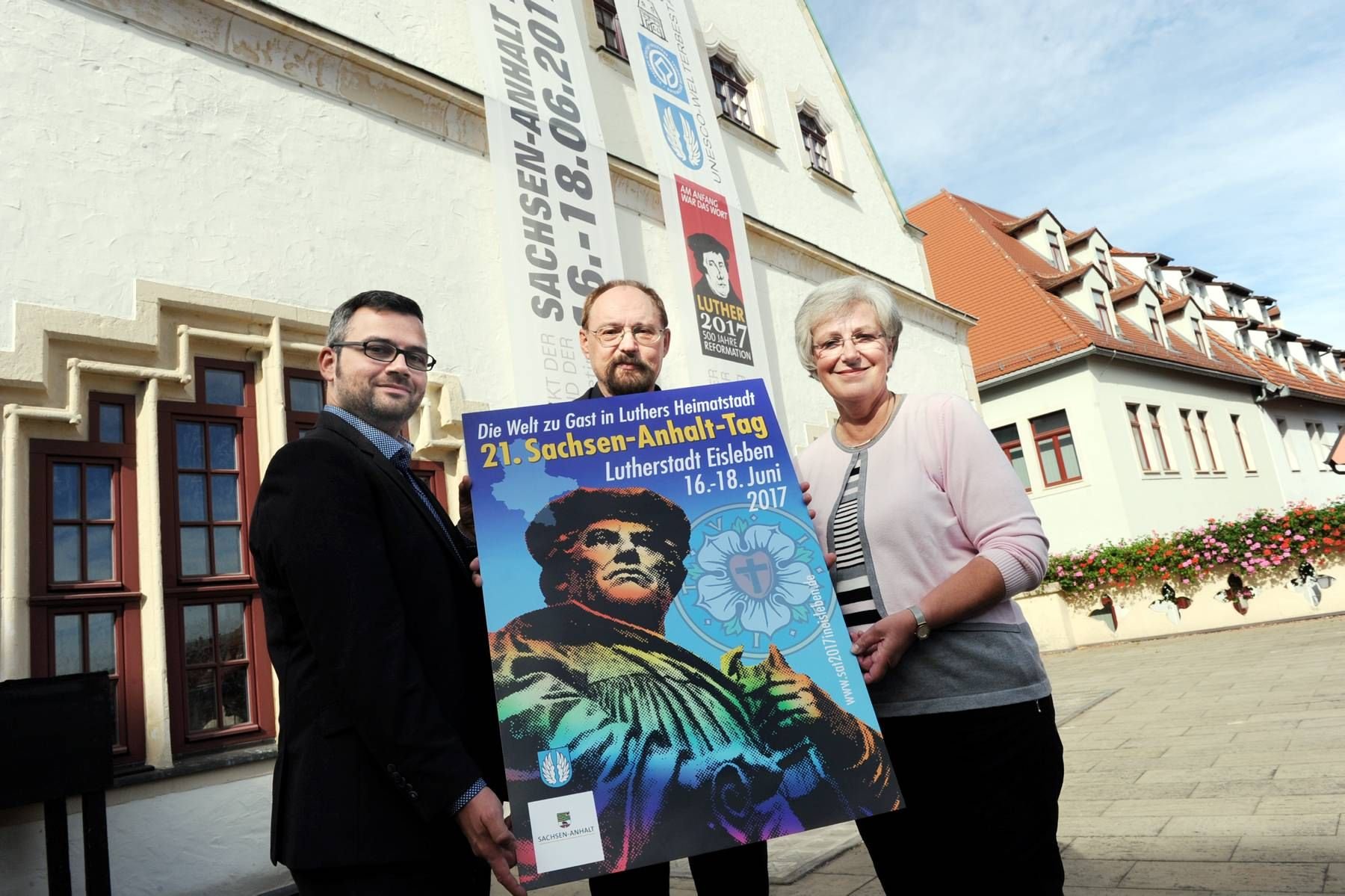 Lutz Döring (Mitte), Sieger des Plakatwettbewerbs für den 21. Sachsen-Anhalt-Tag in Eisleben, präsentiert gemeinsam mit Daniel Mouratidis, stellvertretende Regierungssprecher, und Eislebens Oberbürgermeisterin Jutta Fischer (v.l) das Gewinnerplakat.