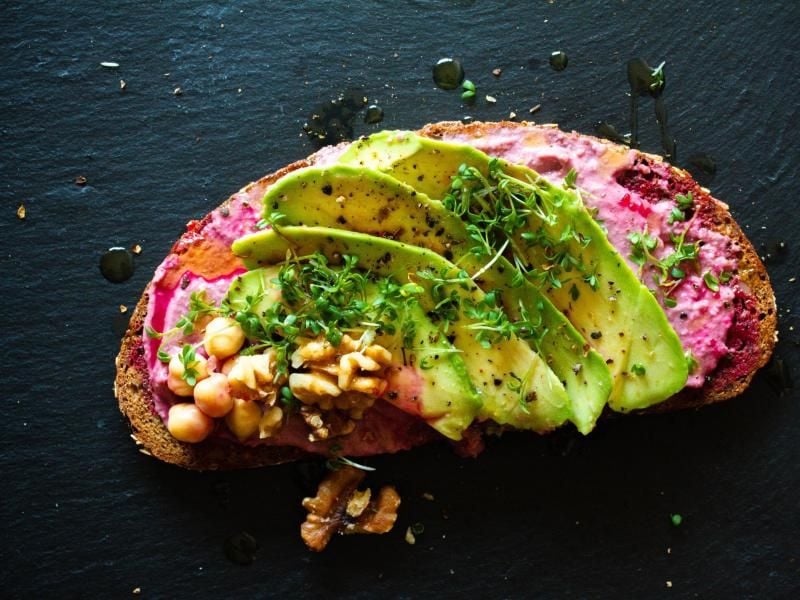 Der Rote Bete Hummus wird auf eine Scheibe Brot gestrichen, mit Avocadoscheiben belegt und mit gehackten Walnüssen, Kresse und Pfeffer bestreut. Foto: Aileen Kapitza/www.minzgruen.com/dpa-tmn