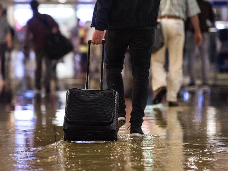 Mann geht mit Koffer durch den unter Wasser stehenden Hauptbahnhof in Hannover. Foto: Silas Stein