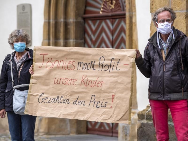 Demonstranten halten während einer Mahnwache zur Situation beim Fleischwerk Tönnies auf dem Marktplatz in Rheda-Wiedenbrück ein Schild mit der Aufschrift „Tönnies macht Profit - unsere Kinder bezahlen den Preis!”. Foto: David Inderlied/dpa