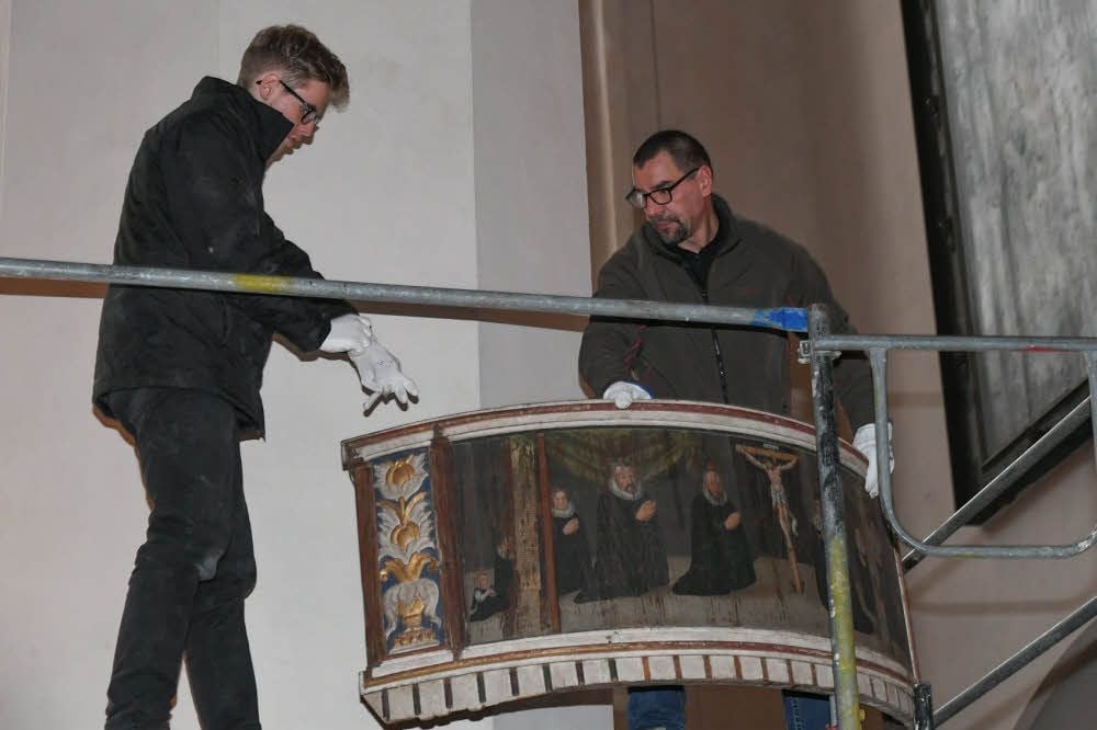 Martin Grünhagen und Friedemann Knappe (v.l.) aus Halle hängen das restaurierte Epitaph an einem Nordpfeiler der Kirche auf.