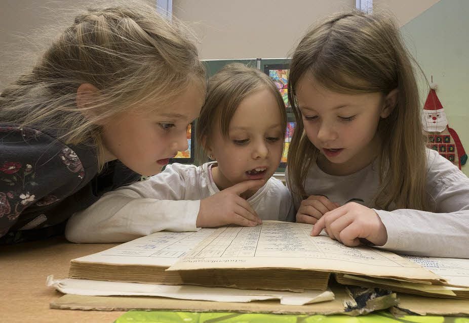 Das ist spannend: In einem Zeugnisbuch von 1950 blättern Charlotte, Kathi und Abi (v.l.) in der Neustädter Grundschule (rechts). Dabei stellen sie fest, dass die heute über 70-Jährigen auch keine besseren Schüler waren. Die heutigen Schüler sind aber bekannt für ihre tollen Theaterstücke. Mit einem davon eröffneten sie die Feierstunde zum 140-jährigen Bestehen ihrer Schule.