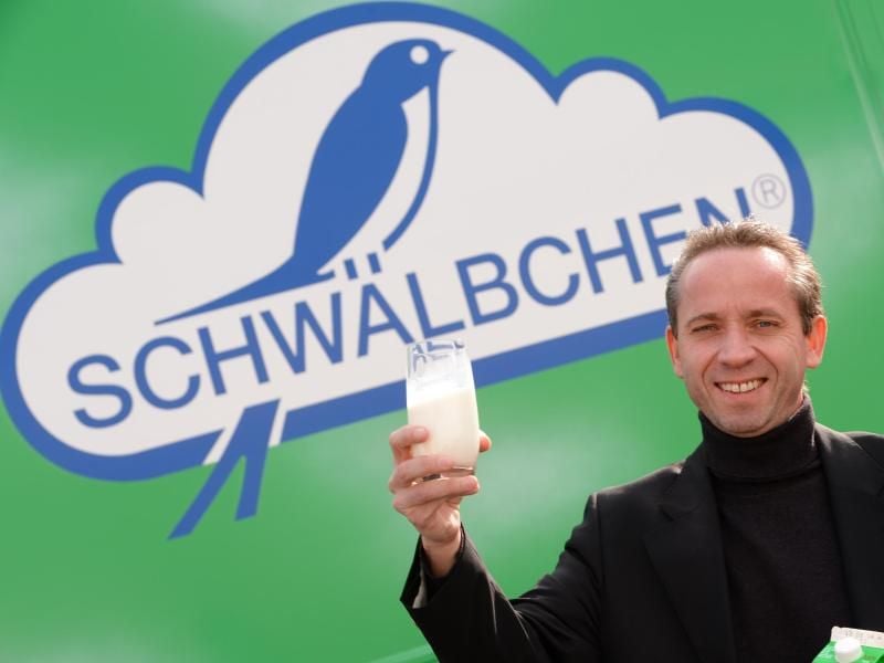 Günter Berz-List, Vorstandsvorsitzender der Schwälbchen Molkerei Jakob Berz AG, steht vor einem Firmenlogo. Foto: Arne Dedert/Archiv