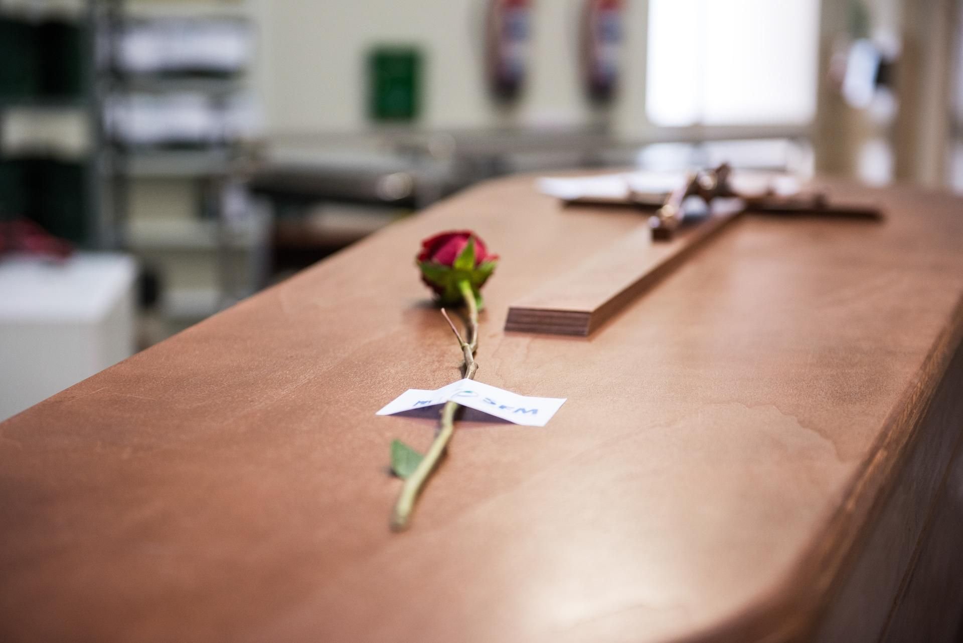 Eine Rose liegt auf einem Sarg, bevor dieser eingeäschert wird.