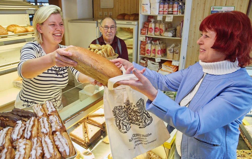 Kerstin Hülße (links) bedient Stammkundin Gisela Möritz. Im Hintergrund hält Gerhard Hülße einen Korb voll leckerer Brötchen in die Höhe.